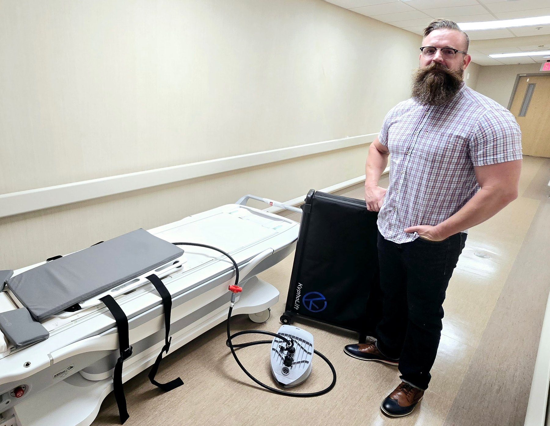 KyphoLift rolling case and foot pump next to an empty MRI table in a hospital corridor