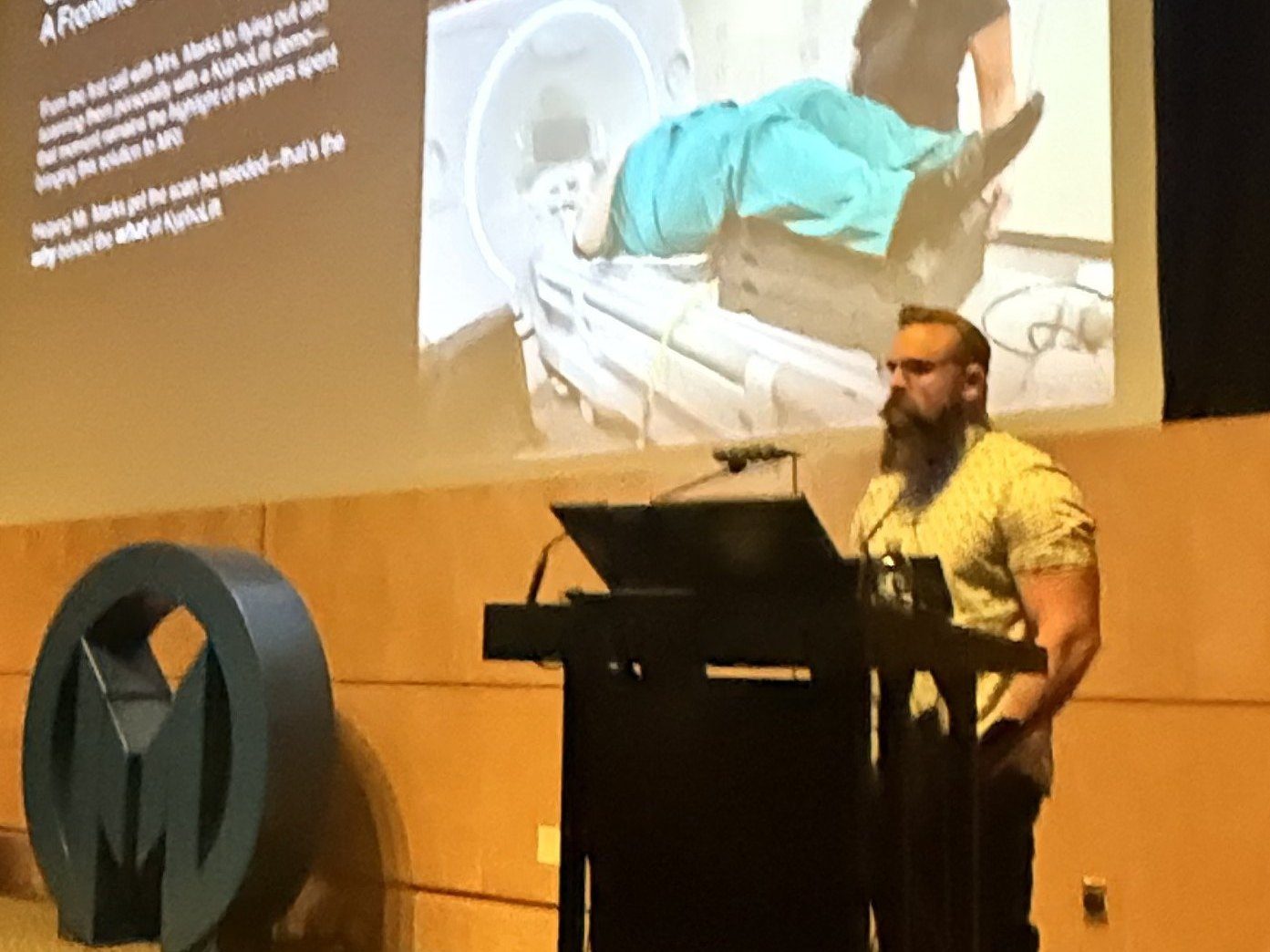 Brandon Johnson presenting When MRI Positioning Becomes a Safety Risk, with photographs of William and Christine Marks on the slide